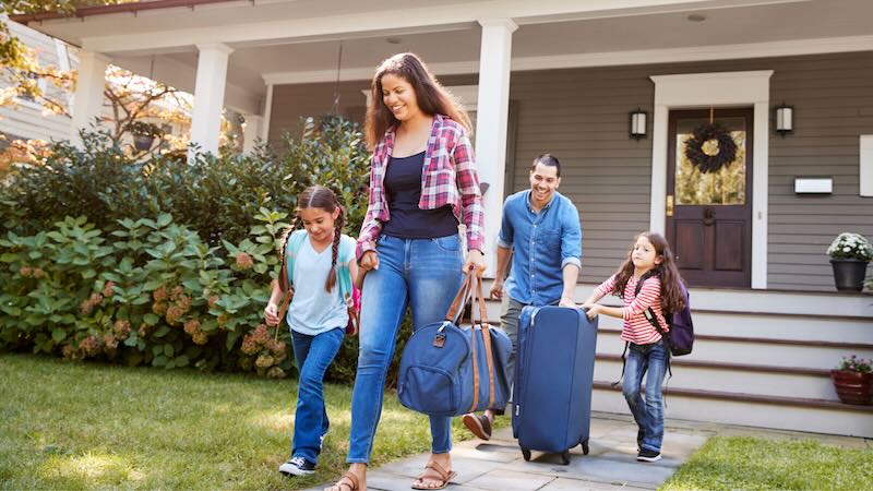 Smiling family leaving their home with cruise luggage, including rolling suitcases and duffel bags. Ready to start their vacation. Best cruise luggage options shown in use.