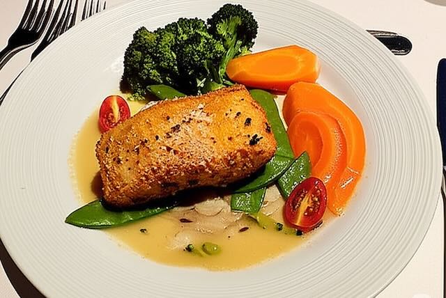 salmon with veggies eating clean on a cruise ship forks on the side with a plate
