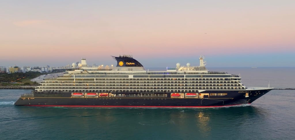 Explora II luxury cruise ship sailing at sunset near a coastal city